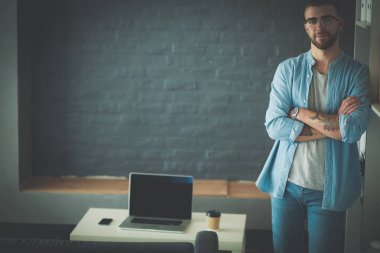 Duvarın yanında dizüstü bilgisayar tutan genç adam..