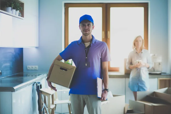 Lachende bezorger in blauw uniform levert pakketdoos aan ontvanger - koerier service concept. Glimlachende bezorger in blauw uniform — Stockfoto