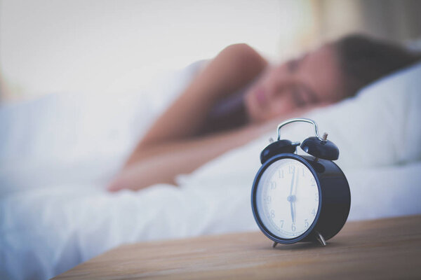 Young sleeping woman and alarm clock in bedroom at home. Young sleeping woman.