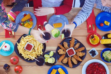 Ahşap masada otururken birlikte yemek yiyen bir grup insanın üst düzey görüntüsü. Masada yemek var. İnsanlar fast food yiyor..