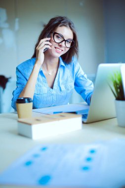 Ofis masasında oturan ve cep telefonuyla konuşan genç ve güzel bir iş kadını. İş kadını