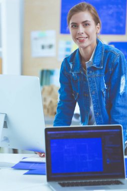 Enstrümanlar, planlar ve dizüstü bilgisayarlarla masanın yanında duran genç bir kadın..