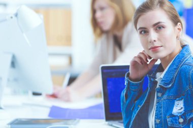 İki genç kadın masada enstrümanlar, planlar ve dizüstü bilgisayarlarla oturuyor..