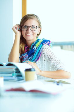 Kitapların arasında bir masada oturan genç bir kadın. Öğrenci