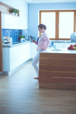 Cep telefonu ayakta modern mutfak kullanan kadın.