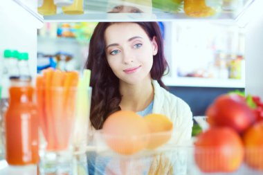 Sağlıklı yiyecek, sebze ve meyvelerle dolu açık buzdolabının yanında duran kadın portresi. Kadın portresi