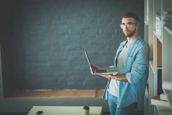 Young man holding laptop standing near wall. — Stock Photo, Image