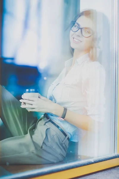 Mujer joven sentada en la mesa de la oficina con portátil, vista a través de la ventana. Mujer joven —  Fotos de Stock