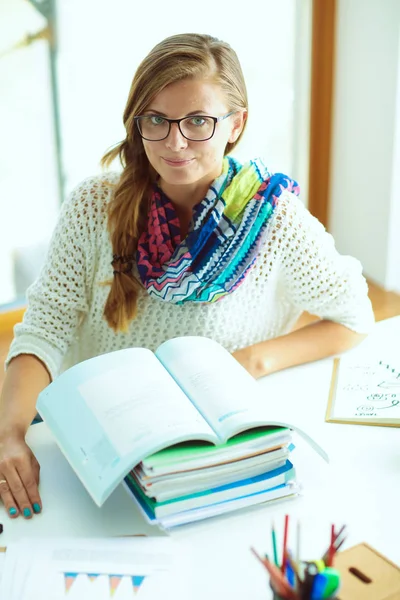 Kitapların arasında bir masada oturan genç bir kadın. Öğrenci