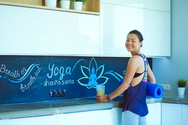 Retrato de una mujer sonriente sosteniendo en su mano una esterilla de yoga mientras estaba de pie en el estudio. Yoga. Una mujer. Bienestar — Foto de Stock