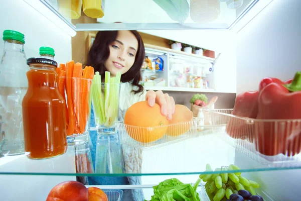 Portrait of female standing near open fridge full of healthy food, vegetables and fruits. Portrait of female — Stock Photo, Image