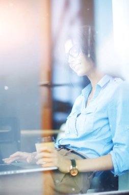 Ofis masasında dizüstü bilgisayarıyla oturan genç bir kadın. Pencereden bakıyor. Genç kadın.