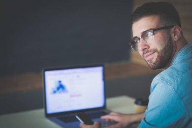 Genç adam kullanarak telefon ve dizüstü bilgisayarda çalışır.