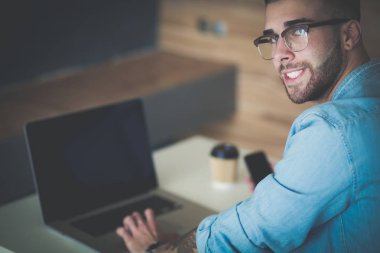 Genç bir telefonu kullanarak ve bir dizüstü bilgisayarda çalışan adam. Öğrenci manifatura telefon.