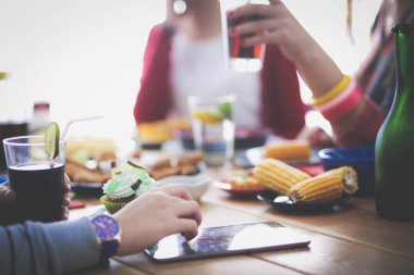 Ahşap masada otururken birlikte yemek yiyen bir grup insanın üst düzey görüntüsü. Masada yemek var. İnsanlar fast food yiyor..