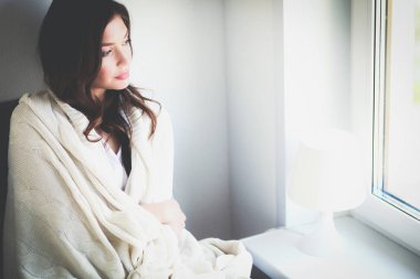 Genç kadın evde oturma odası okuma kitabında rahatlatıcı ve kahve veya çay içme pencere oturuyor. Genç kadın evde