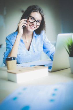 Ofis masasında oturan ve cep telefonuyla konuşan genç ve güzel bir iş kadını. İş kadını