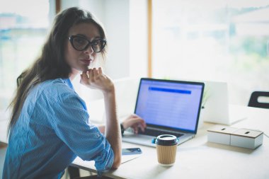 Ofis masasında oturan genç bir kadın dizüstü bilgisayar ekranına bakıyor. Genç kadın.
