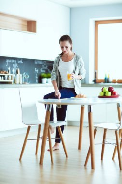 Mutfakta portakal suyu ve tableti olan genç bir kadın..