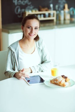 Mutfakta portakal suyu ve tableti olan genç bir kadın..