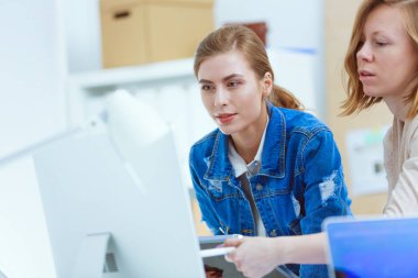 Masanın yanında duran iki genç kadın enstrüman, plan ve dizüstü bilgisayarla.