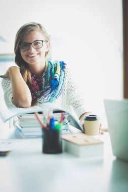 Kitapların arasında bir masada oturan genç bir kadın. Öğrenci