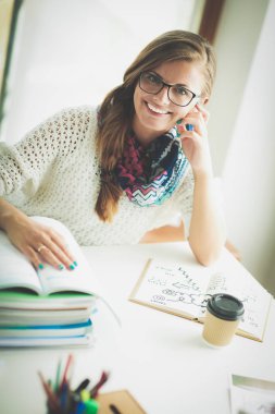 Kitapların arasında bir masada oturan genç bir kadın. Öğrenci