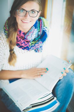 Kitapların arasında bir masada oturan genç bir kadın. Öğrenci
