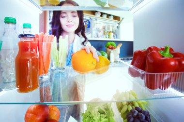 Sağlıklı yiyecek, sebze ve meyvelerle dolu açık buzdolabının yanında duran kadın portresi. Kadın portresi