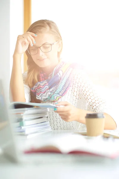 Jonge vrouw zit achter een bureau tussen de boeken. Studenten — Stockfoto