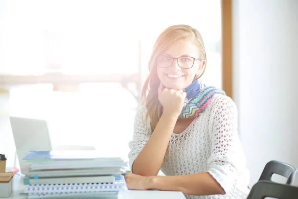 Giovane donna seduta ad una scrivania tra i libri. Studente — Foto Stock