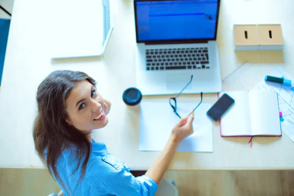 Jovem sentada à mesa do escritório com laptop, vista pela janela. Jovem mulher — Fotografia de Stock