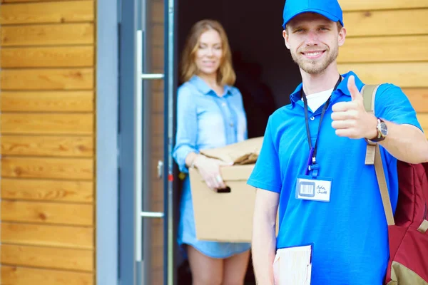 Repartidor sonriente con uniforme azul que entrega la caja de paquetes al destinatario: concepto de servicio de mensajería. Repartidor sonriente en uniforme azul —  Fotos de Stock