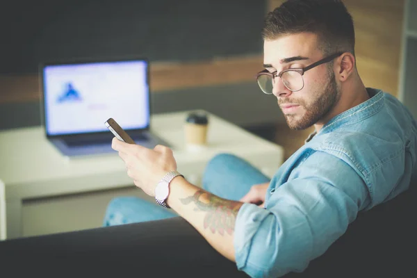 Ung man använder telefonen och fungerar på den bärbara datorn. — Stockfoto