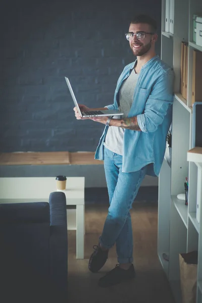 Young man holding laptop standing near wall. — Stock Photo, Image