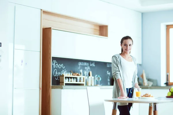 Mujer joven con jugo de naranja y tableta en la cocina. — Foto de Stock