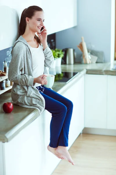현대 부엌에 앉아 휴대 전화를 사용 하 여 여자. — 스톡 사진
