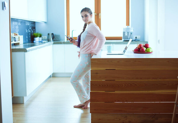 Woman using mobile phone standing in modern kitchen.