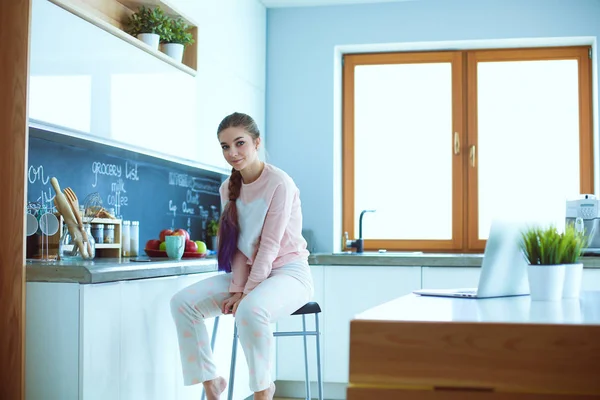 Ung kvinna sitter på bord i köket. — Stockfoto