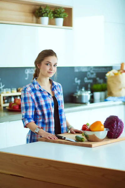 Masanın yanındaki mutfakta sebze doğrayan genç bir kadın..