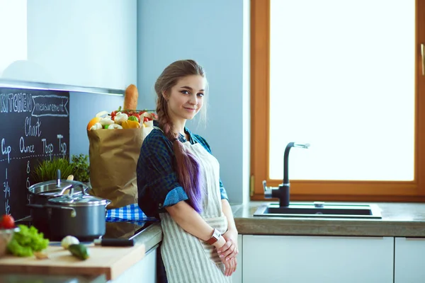 Egy fiatal nő áll a tűzhely mellett a konyhában. . — Stock Fotó