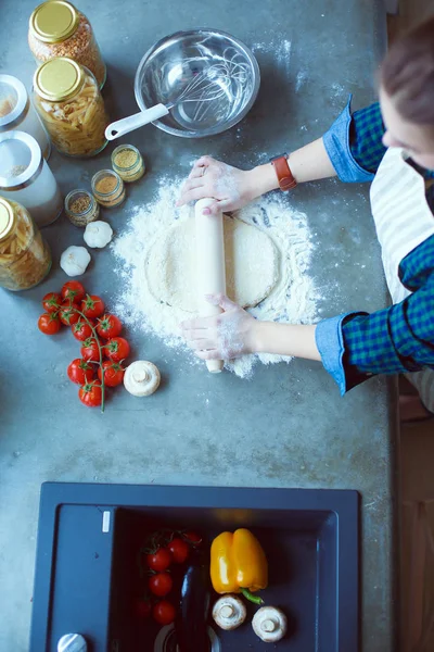 Güzel bir kadın mutfakta pasta pişiriyor. Masanın yanında duruyor..