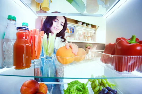 Sağlıklı yiyecek, sebze ve meyvelerle dolu açık buzdolabının yanında duran kadın portresi. Kadın portresi
