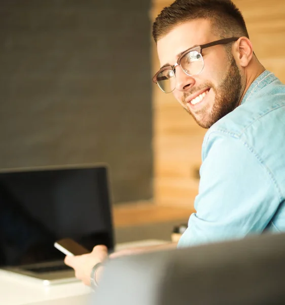 Jonge man met telefoon en werkt op de laptop — Stockfoto