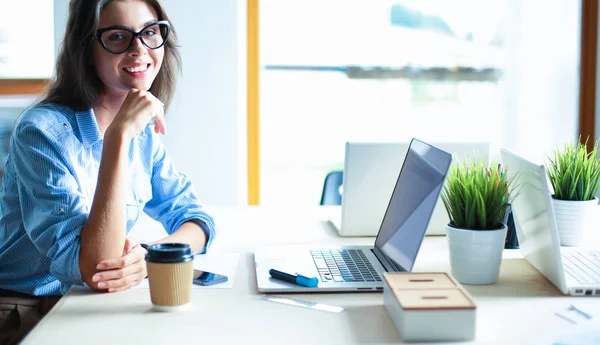 Ofis masasında dizüstü bilgisayarıyla oturan genç bir kadın.