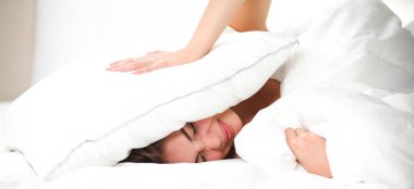 Kadın yatakta uzanıyor ve kulaklarını yastıkla kapatıyor.