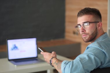 Genç adam kullanarak telefon ve dizüstü bilgisayarda çalışır.