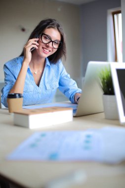 Ofis masasında oturan ve cep telefonuyla konuşan genç ve güzel bir iş kadını. İş kadını