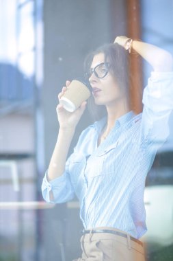 Ofis masasında dizüstü bilgisayarıyla oturan genç bir kadın. Pencereden bakıyor. Genç kadın.