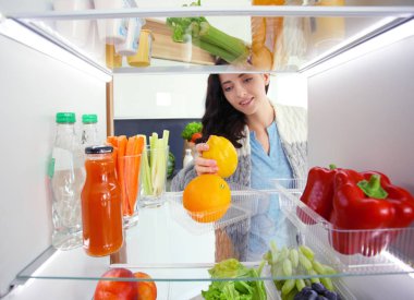 Sağlıklı yiyecek, sebze ve meyvelerle dolu açık buzdolabının yanında duran kadın portresi. Kadın portresi